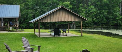 A covered outdoor seating area with Adirondack chairs, a grill, and a table set up for dining.