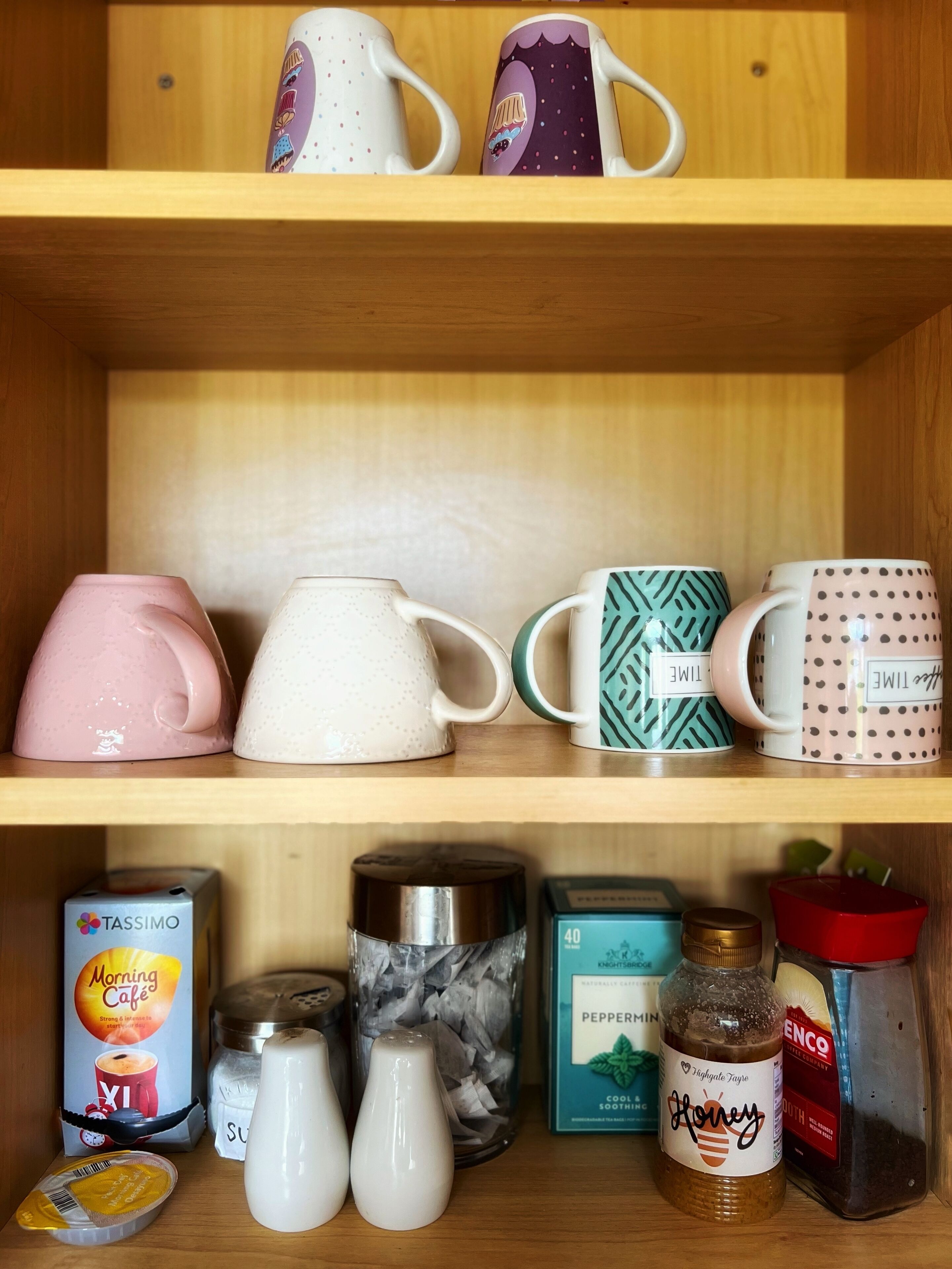 A shelf with various kitchen items including mugs, a coffee maker, and condiments.