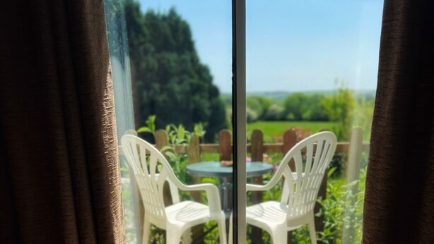 A modern room with a black rocking chair, a wooden floor, and a view of a garden through a glass door. - Private small house in Cork countryside [Springfiled] (Minane Bridge)
