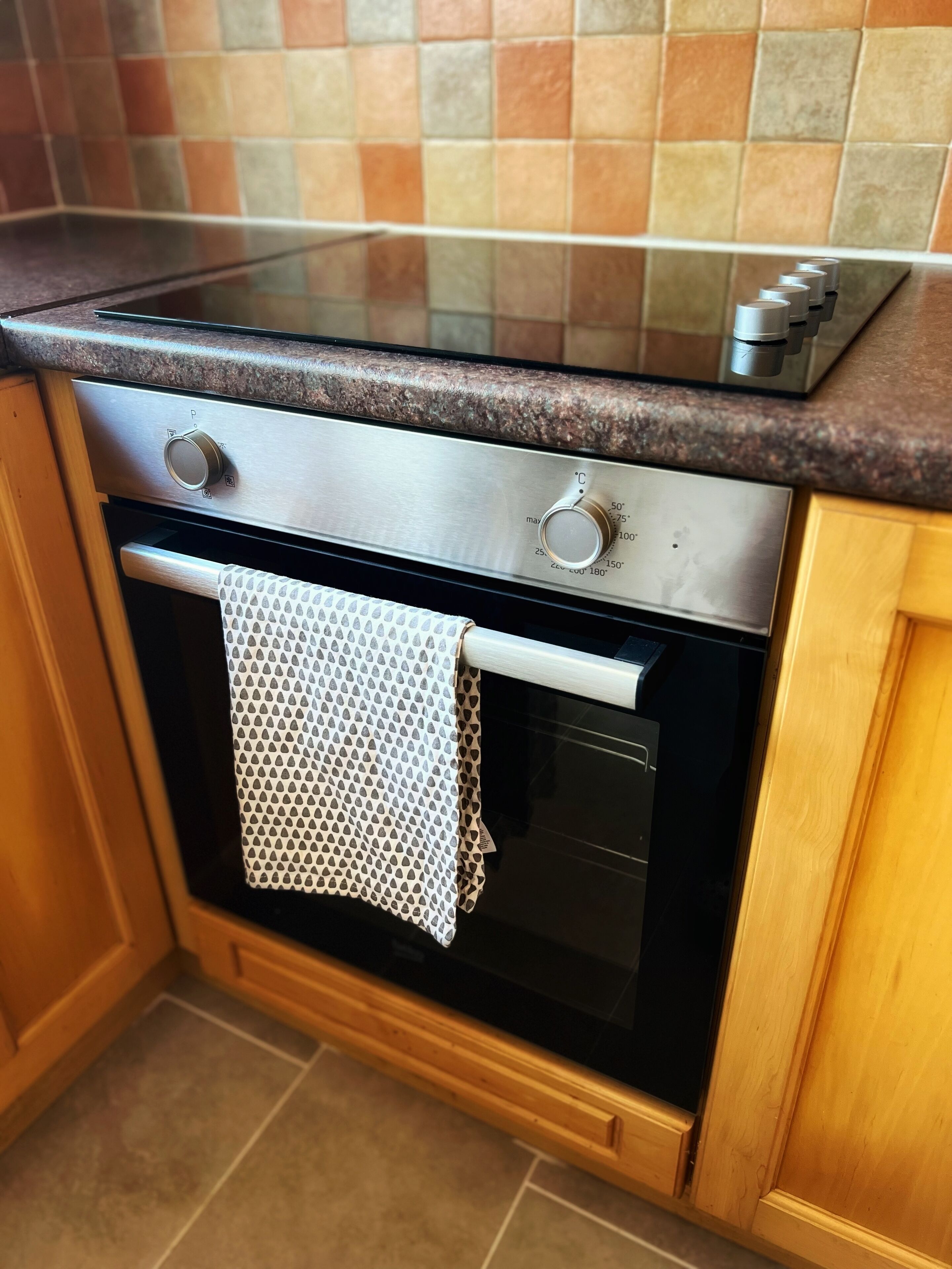 Eine Küche mit einem Edelstahlbackofen, einer Mikrowelle und einem gemusterten Handtuch, das an der Backofentür hängt.