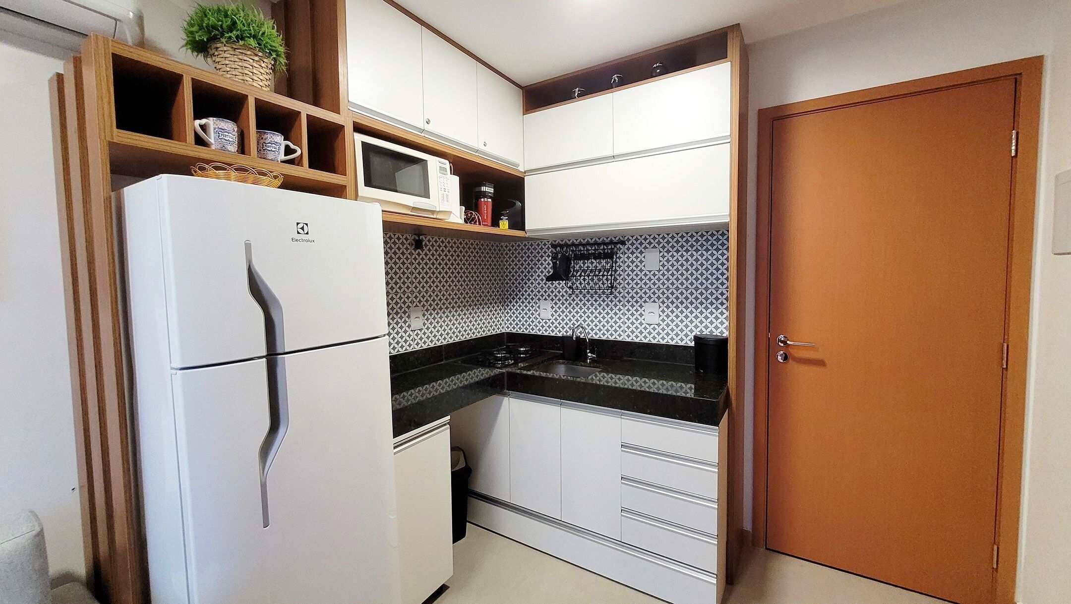 Cocina compacta con refrigerador blanco, microondas y estufa. Cuenta con gabinetes de madera y salpicadero de azulejos.
