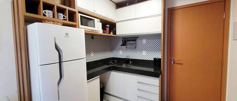 Cocina compacta con refrigerador blanco, microondas y estufa. Cuenta con gabinetes de madera y salpicadero de azulejos.