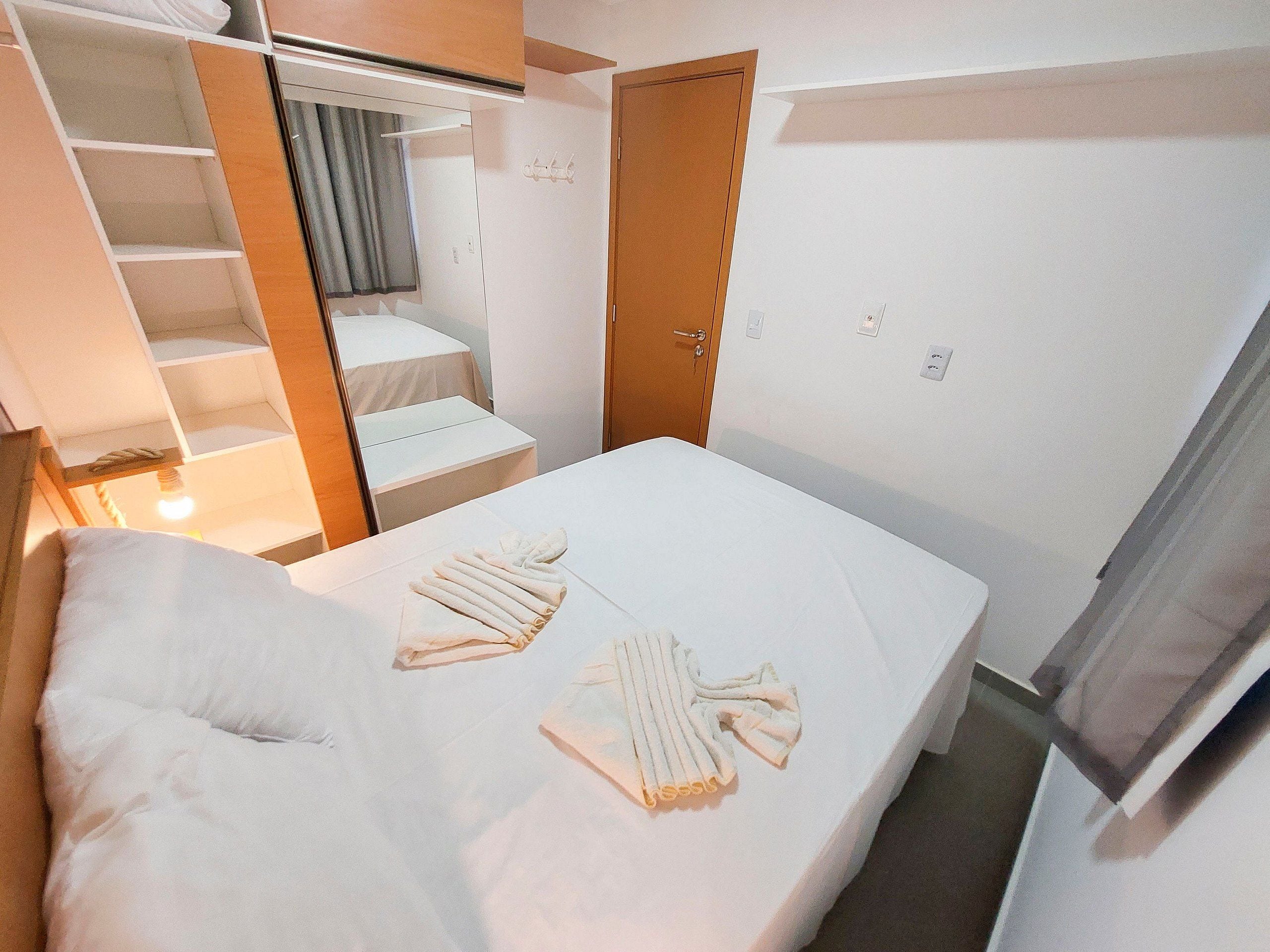 A hotel room with a bed, a wardrobe, a small table, and a mirror.