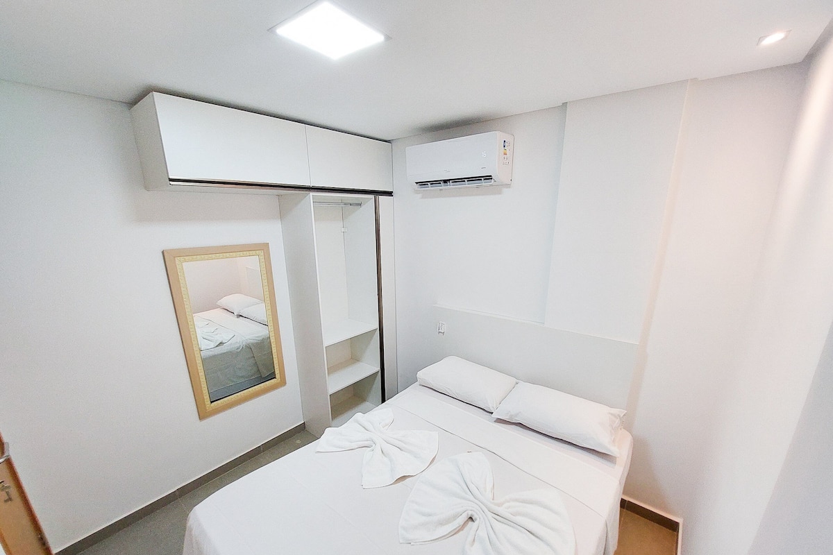 A hotel room with a bed, a mirror, a wardrobe, and an air conditioning unit.