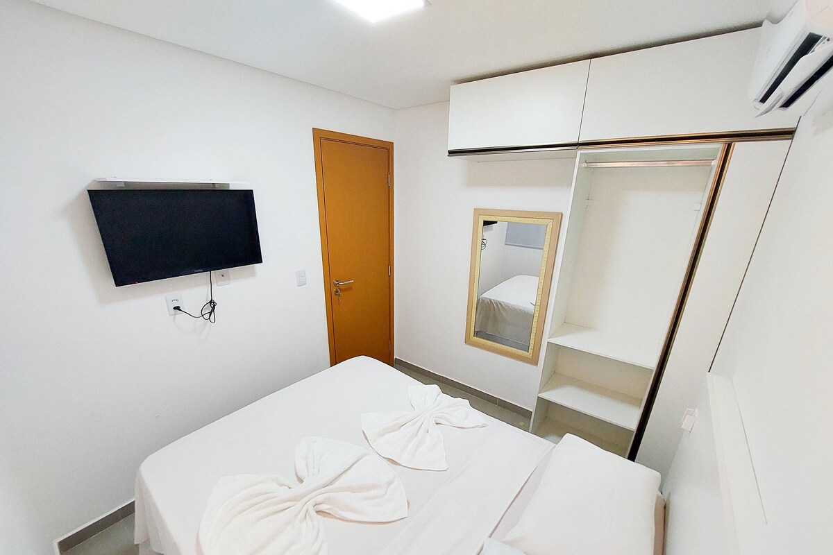 A hotel room with a bed, a television mounted on the wall, a door, and a mirror.