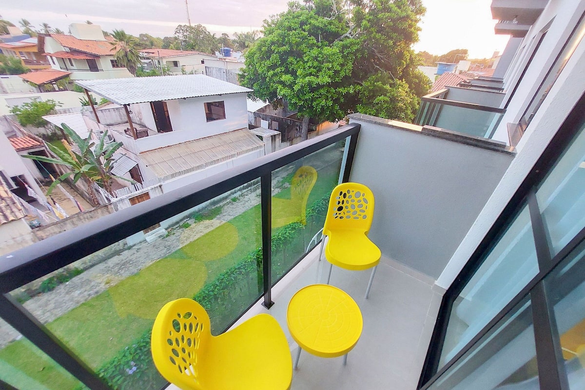 A balcony with yellow chairs and a small table, overlooking a residential area with houses and trees.