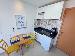 Een kleine keuken met een magnetron, spoelbak en een kleine koelkast. Er is een eettafel met stoelen en een lijst aan de muur.