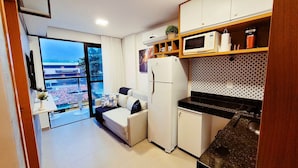 A compact kitchen with a refrigerator, microwave, and a small dining area with a sofa. - Lindos Flats - Maraca Beach Residence II (Ipojuca)