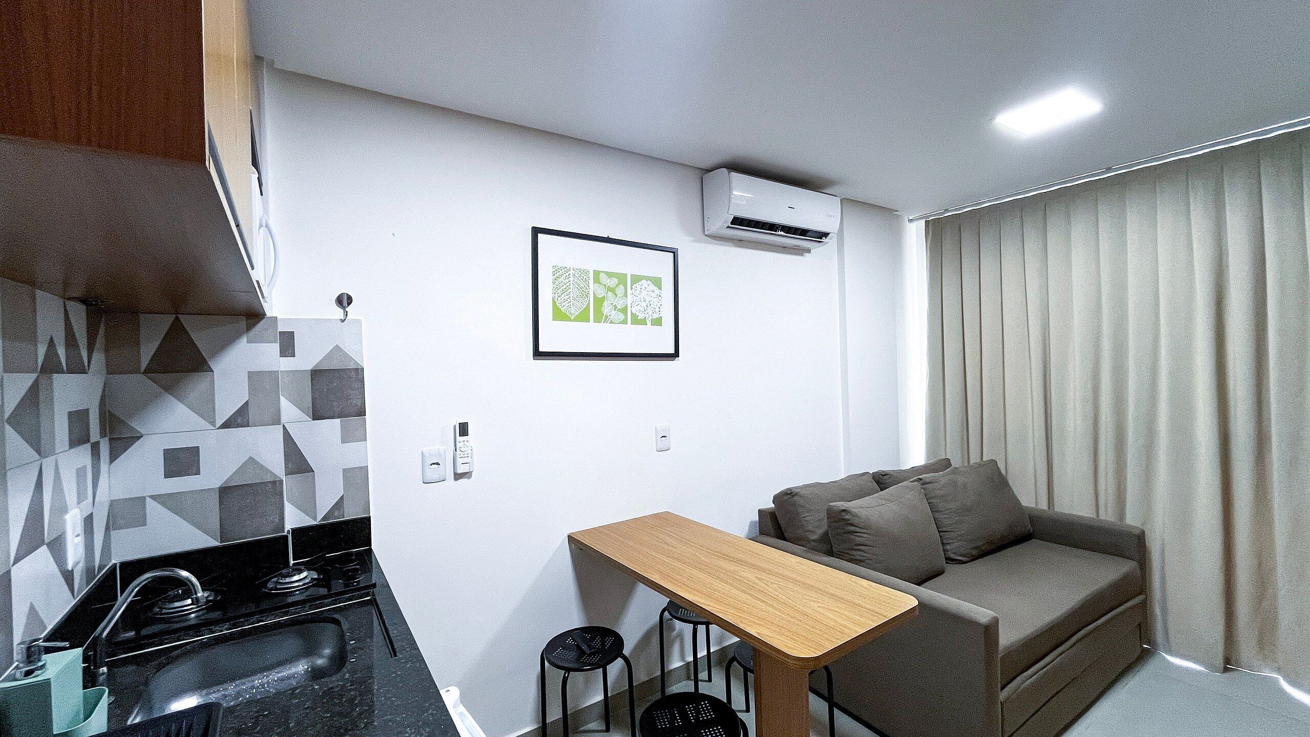 A compact living space with a kitchenette, a sofa, a small wooden table, and a framed botanical print on the wall.