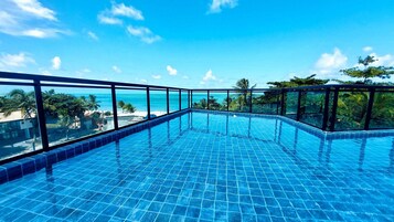A clear blue infinity pool with a glass balustrade, surrounded by lush greenery and a view of the ocean.