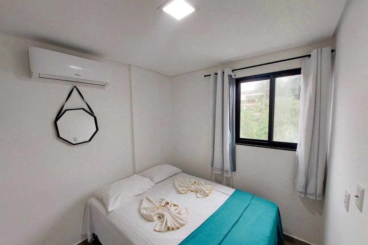 A single bed with a teal bedspread and two towels arranged on it.