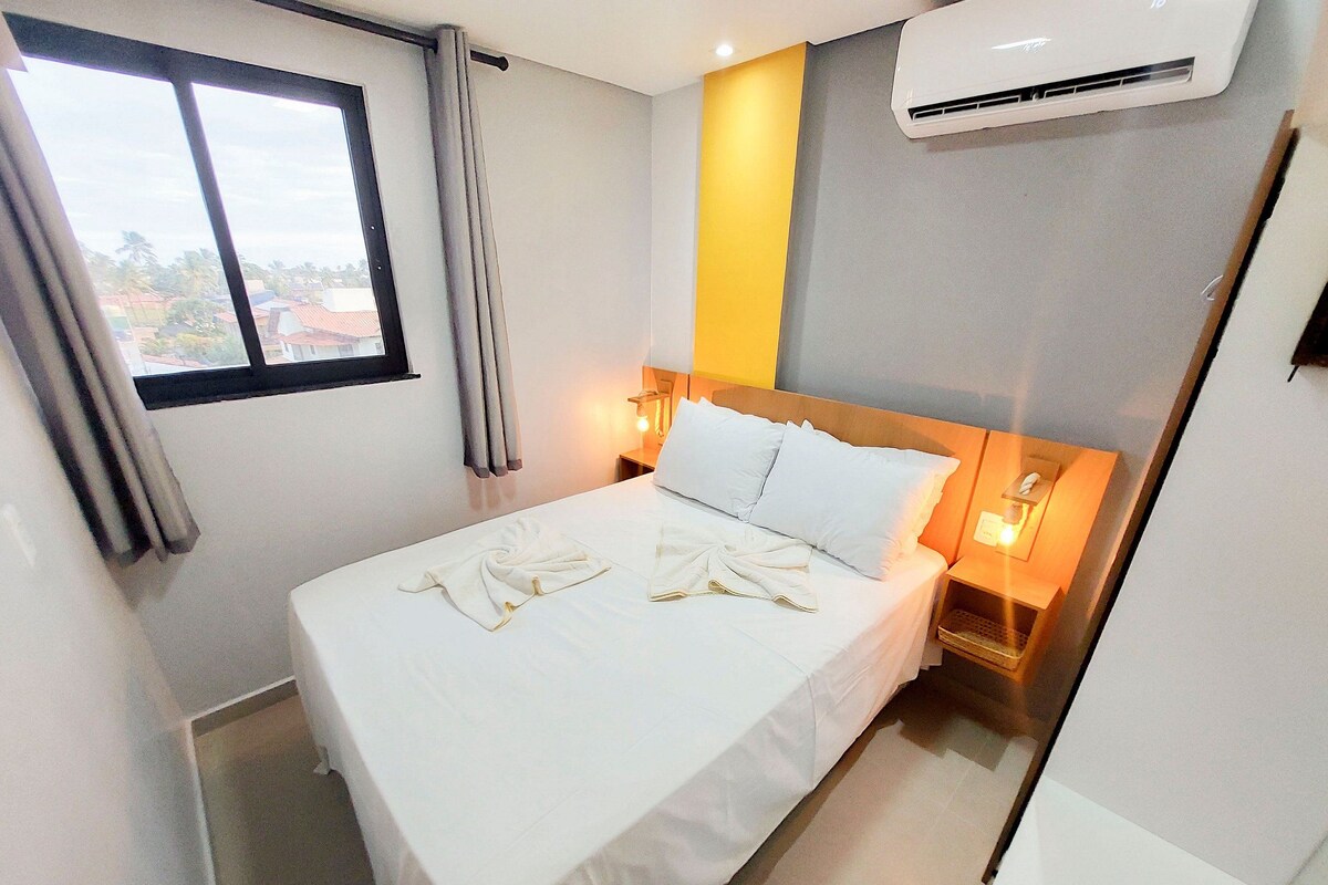 A hotel room with a bed, curtains, an air conditioning unit, and a window.