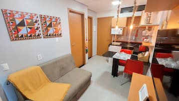 Un espacio habitable compacto con sofá, mesa de comedor, sillas, zona de cocina y obras de arte en las paredes.