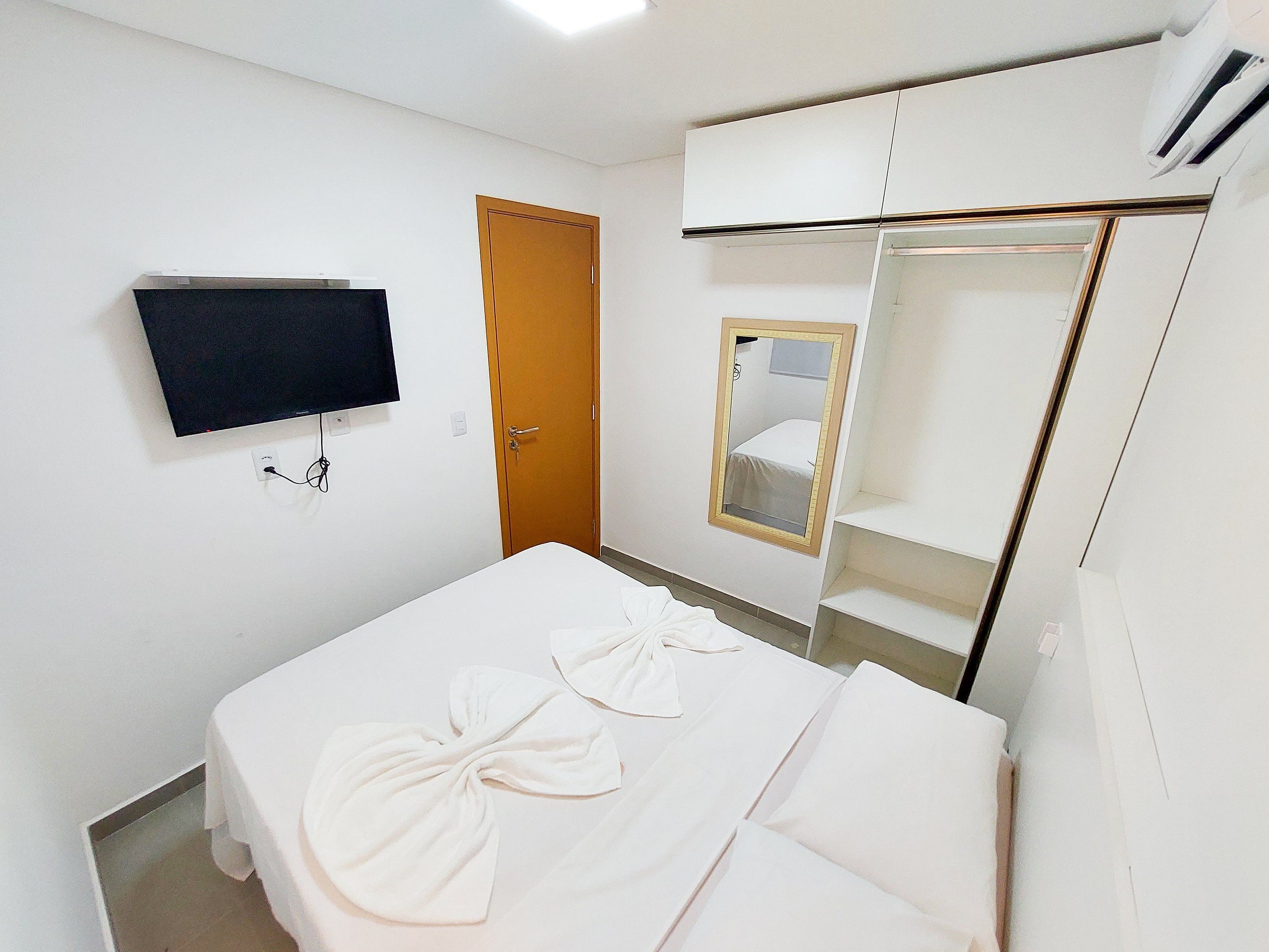 Una habitación de hotel con una cama, un televisor montado en la pared, una puerta y un espejo.