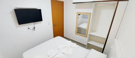 Una habitación de hotel con una cama, un televisor montado en la pared, una puerta y un espejo.