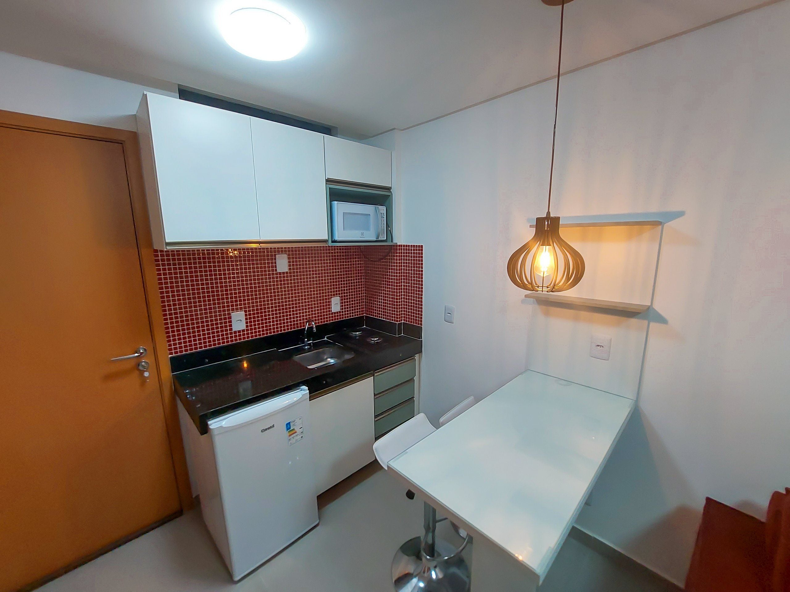 A compact kitchen with white cabinets, a microwave, a sink, and a hanging light fixture.