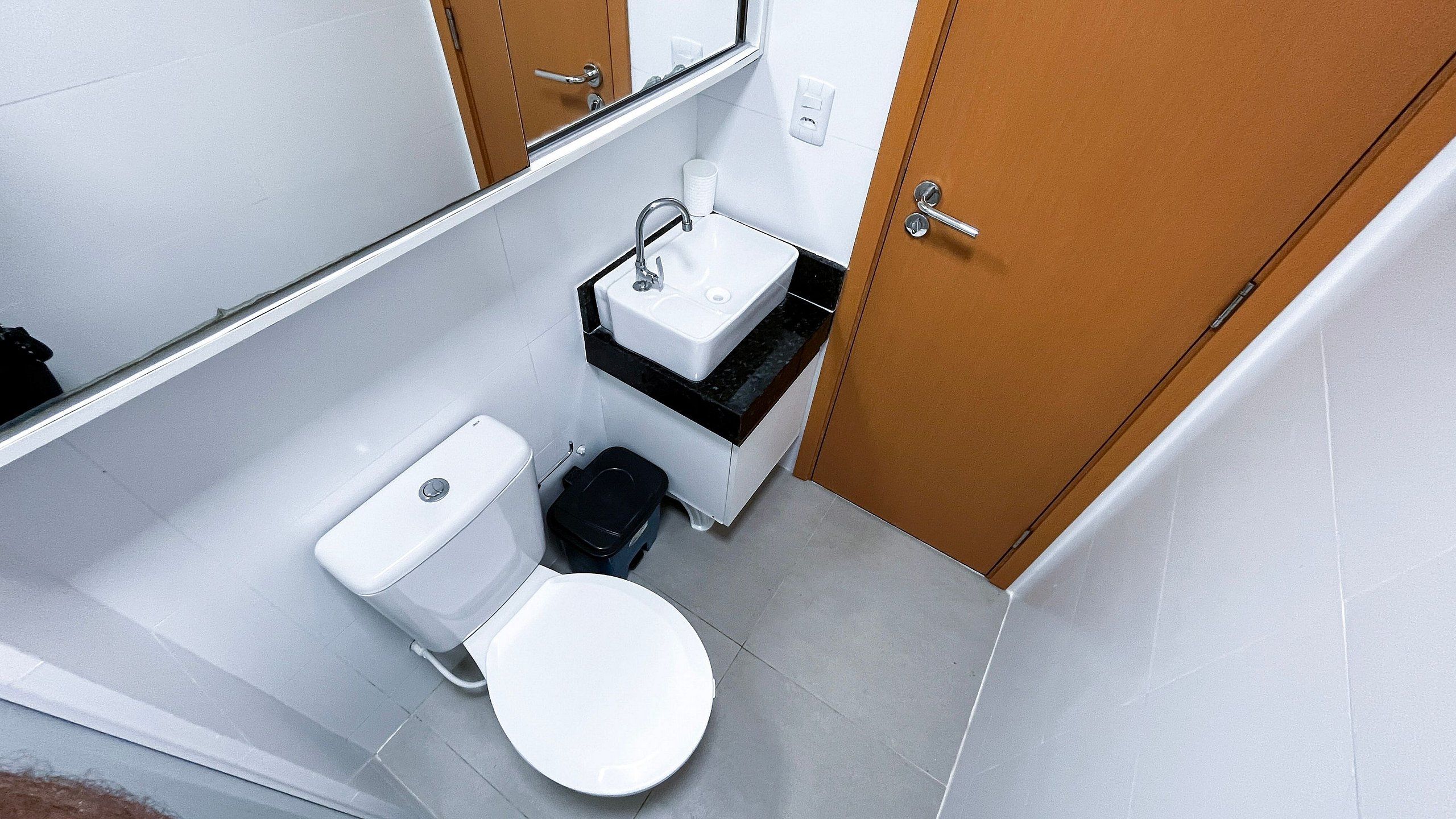 A compact bathroom with a toilet, sink, and a small trash bin.