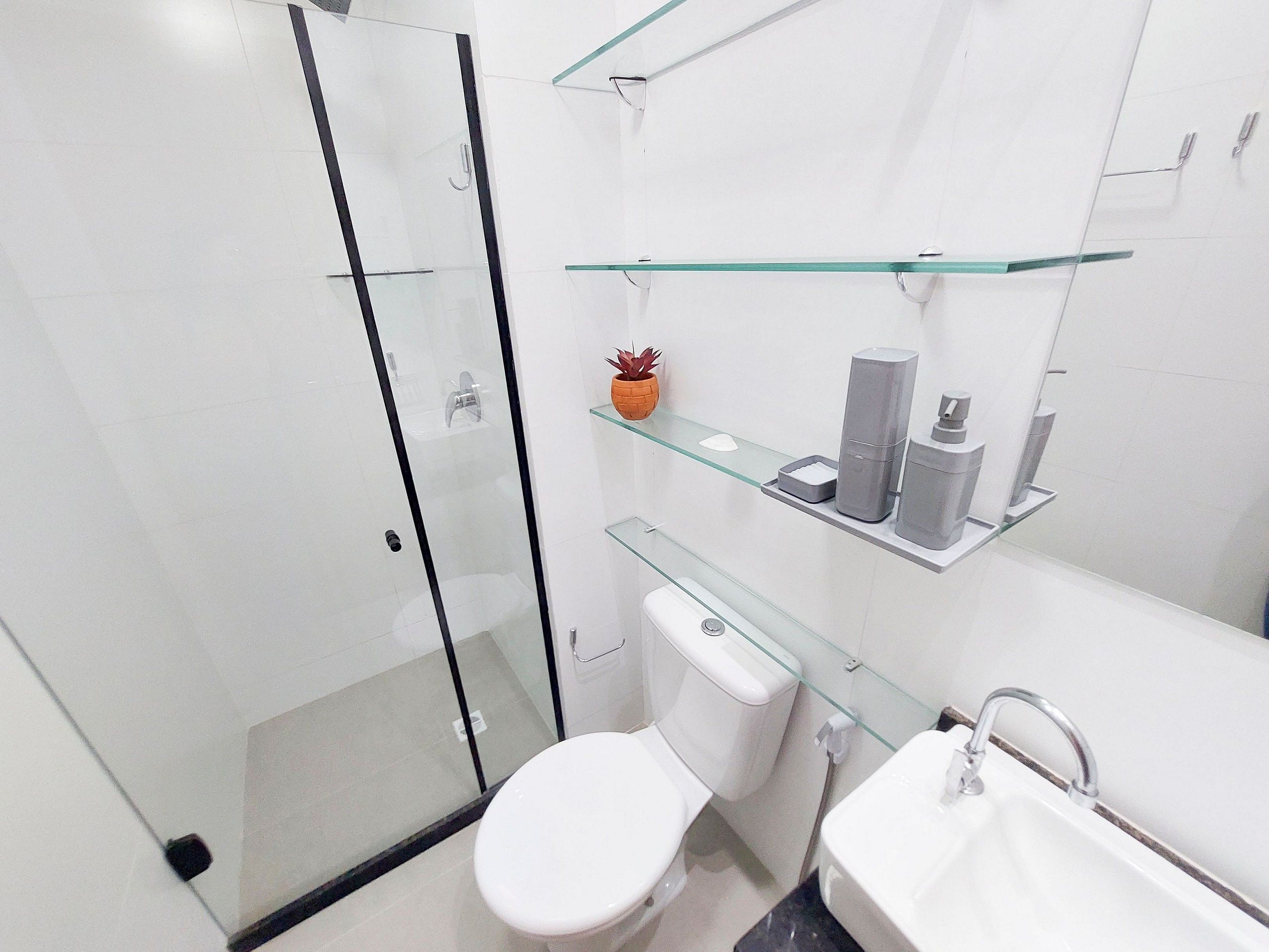 Une salle de bain moderne avec une douche à parois de verre, des toilettes, un lavabo avec un miroir et des étagères en verre où sont rangés les articles de toilette.