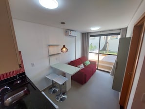 En kompakt opholdsstue med et tekøkken, spiseplads, en rød sofa og en stor skydedør, der fører til et udendørs område.