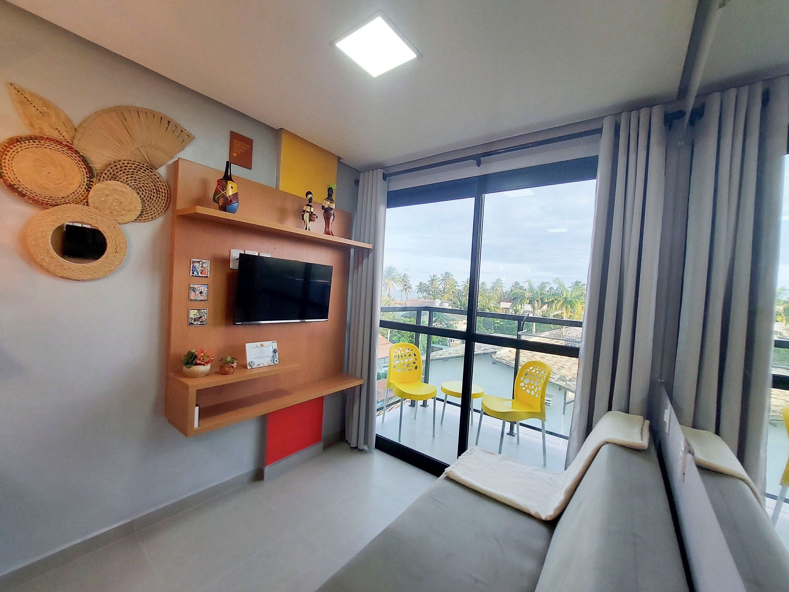 Un salon moderne avec un téléviseur à écran plat, un canapé et un balcon agrémenté de chaises jaunes.