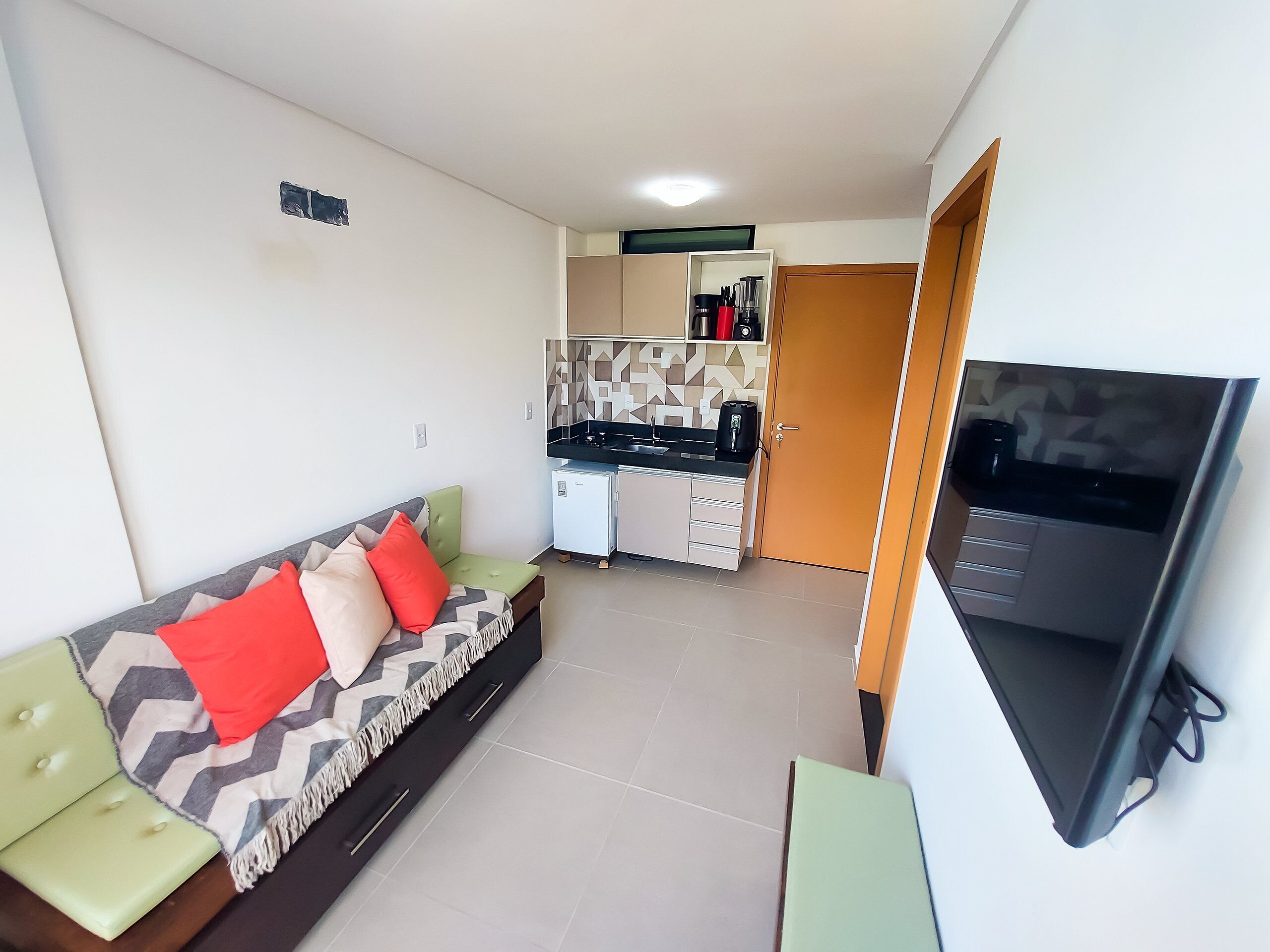 A compact living space with a sofa, kitchenette, and a TV.