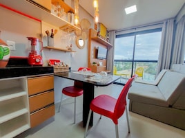 A modern kitchen with a dining area, a red blender, and a large window with a view.