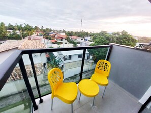 Een balkon met twee gele stoelen en een glazen hekwerk met uitzicht op een woongebied met huizen en palmbomen.