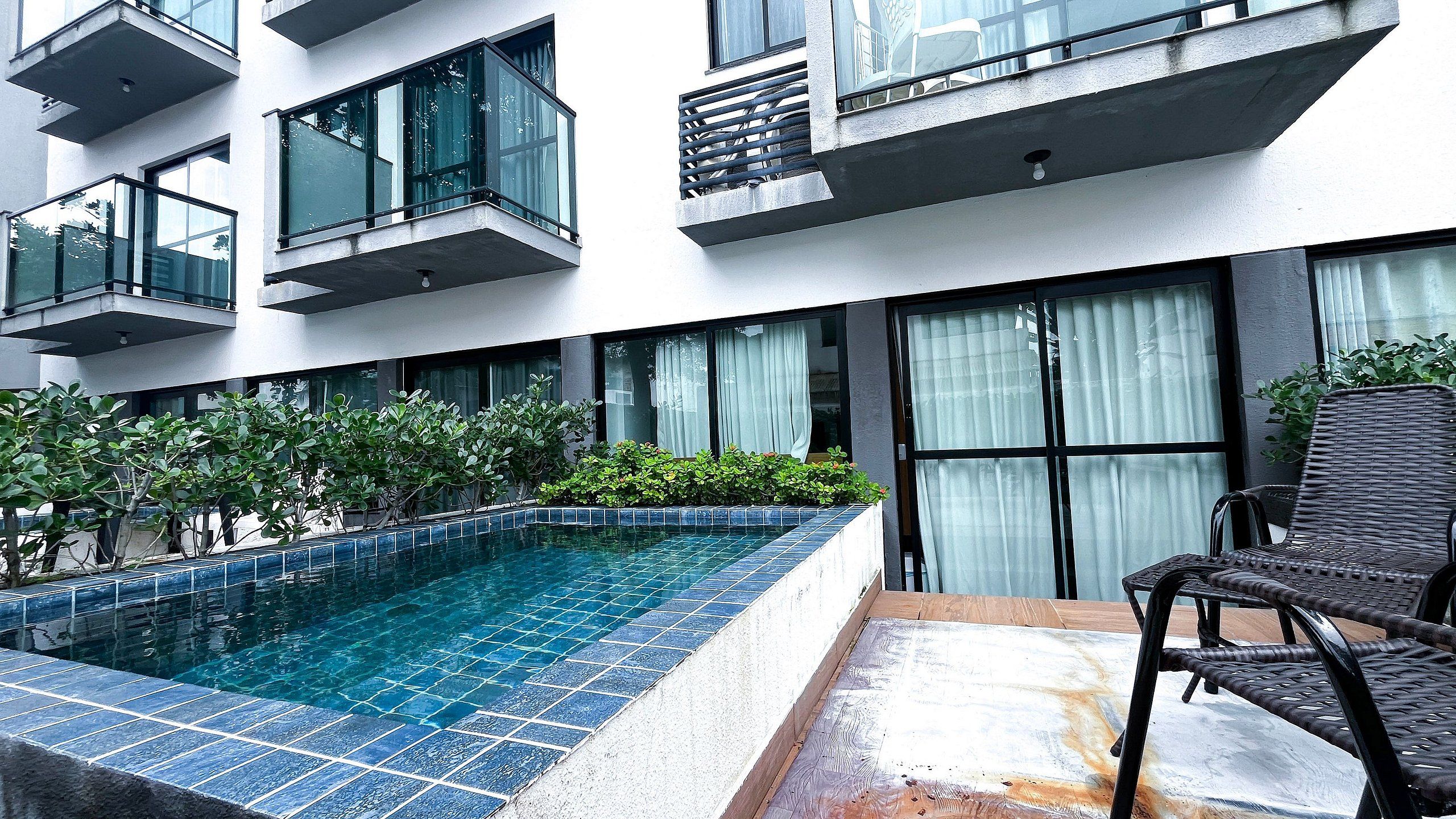 A modern building with a swimming pool, outdoor seating, and greenery.