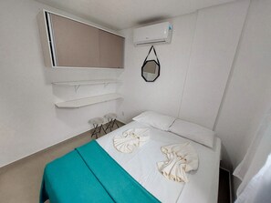 Een hotelkamer met een bed, een spiegel, een plank en een airconditioning.