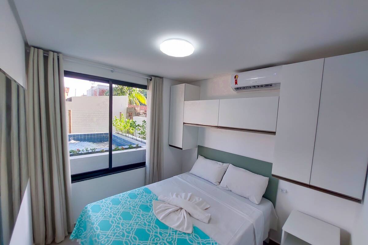 A hotel room with a bed, a window with curtains, an air conditioning unit, and a view of a swimming pool.