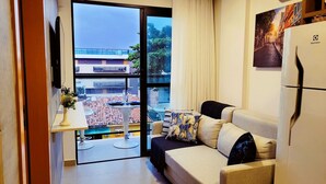 A compact living space with a sofa, a small table, a TV, and a refrigerator. - Lindos Flats - Maraca Beach Residence II (Ipojuca)