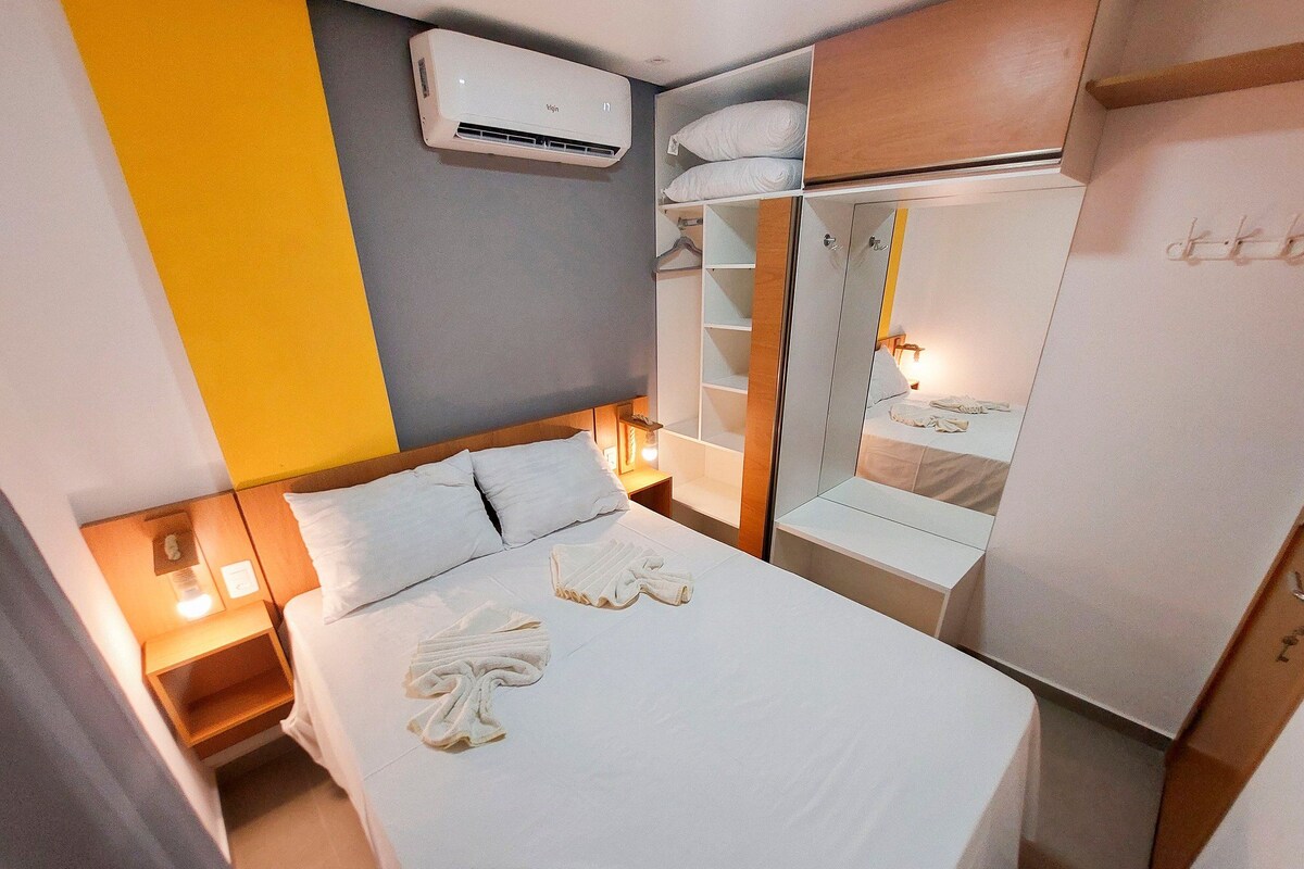 A hotel room with a bed, bedside tables, an air conditioning unit, a wardrobe, and a mirror.