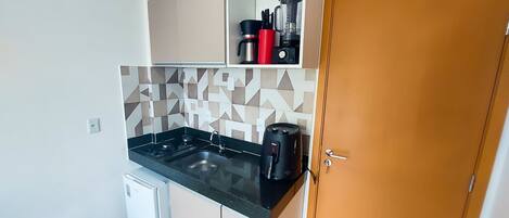A compact kitchen with a black countertop, a coffee maker, and a small refrigerator.