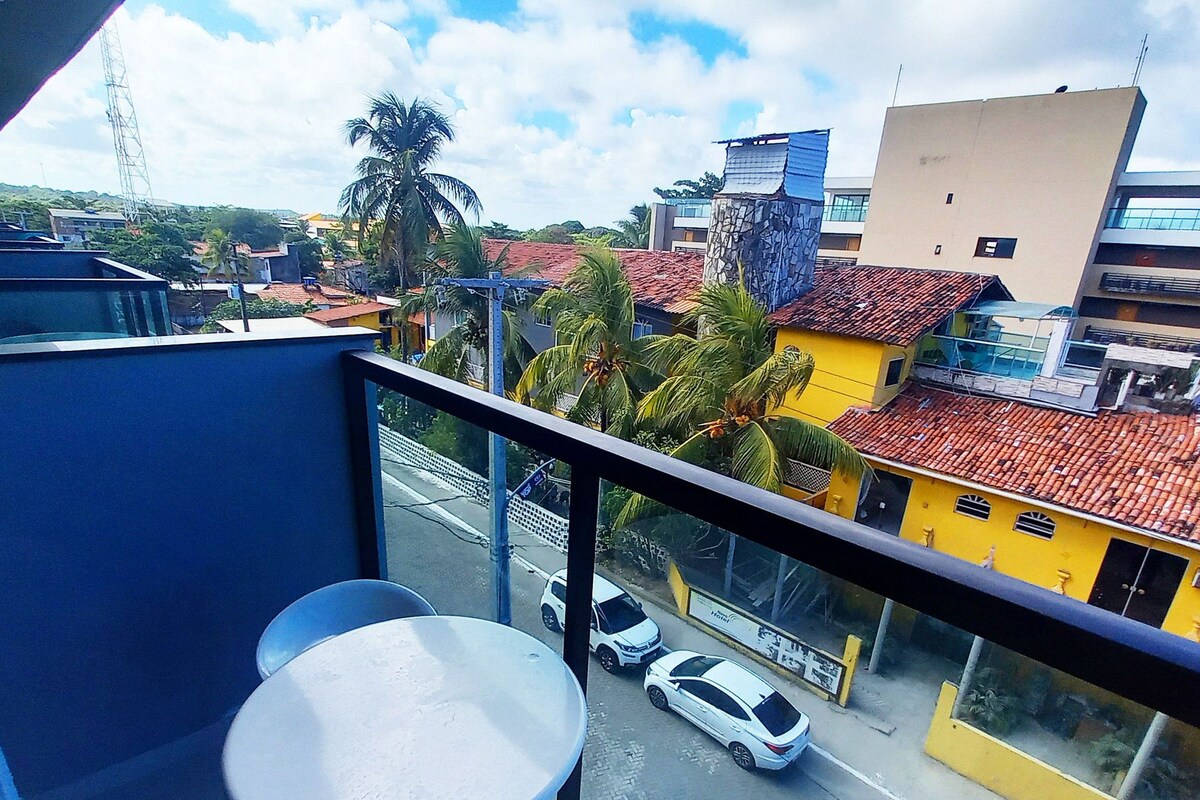 A balcony with two white round tables and chairs, overlooking a street with cars and buildings.