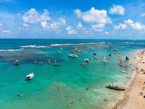 Uma praia com águas turquesa cristalinas, barcos e pessoas.