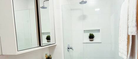 Een moderne badkamer met een douchecabine van glas, een wit toilet, een wastafel met glazen blad en een grote spiegel.