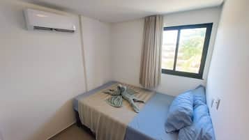 Una habitación pequeña con cama individual, ventana, aire acondicionado de pared y luz en el techo.