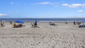 A beach with several sun loungers and umbrellas, a few people walking, and a clear view of the ocean. - Ocean Links - Stunning 3rd Floor Ocean View! (Hilton Head)