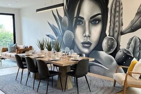 Zona pranzo con tavolo apparecchiato per quattro, circondato da sedie e un grande affresco sulla parete.