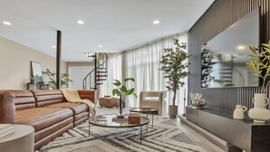 A modern living room with a leather sofa, a coffee table, and a large flat-screen TV. - Stunning 2 Story Villa with Pool (Wilton Manors)