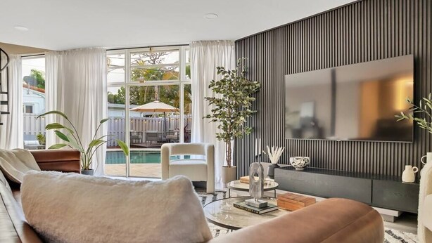 A modern living room with a large TV, comfortable seating, and a view of the outdoors. - Stunning 2 Story Villa with Pool (Wilton Manors)