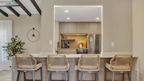 A modern kitchen with four wicker bar stools, a built-in refrigerator, and a small island with a coffee machine. - Stunning 2 Story Villa with Pool (Wilton Manors)