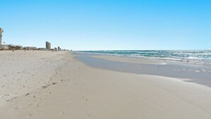 A wide sandy beach with gentle waves, a clear sky, and buildings in the background. - Gulf views! Spacious with 2 King beds, Bunk Room | 5 Pools (Panama City Beach)