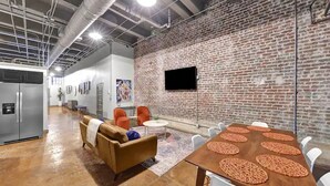 A modern interior with a brick wall, a flat-screen TV, a wooden table with placemats, and a seating area with a sofa and chairs. - Penthouse Loft Downtown Huge Unit (Birmingham)