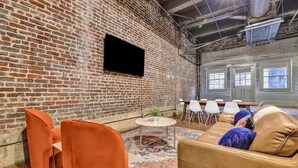 A room with brick walls, a flat-screen TV mounted on the wall, a round table with chairs, and a sofa with cushions. - Penthouse Loft Downtown Huge Unit (Birmingham)