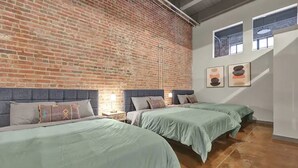 A room with two beds, a brick wall, and a window with artwork. - Penthouse Loft Downtown Huge Unit (Birmingham)