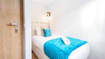 Un dormitorio moderno con cama, lámpara de noche y puerta de madera.