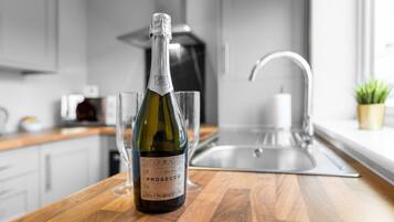 A bottle of Prosecco wine on a wooden countertop in a modern kitchen with a stainless steel sink and a potted plant.