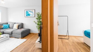 A modern living room with a grey sectional sofa, a white rug, a wooden floor, a black TV stand, and a framed picture on the wall. - Brand New - Two Bed - Parking - Stourbridge (West Midlands)