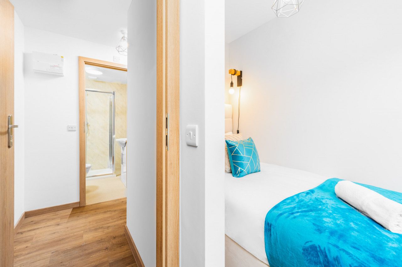 Ein Hotelzimmer mit Holzboden, einem Bett mit blauer Decke und blauem Kopfkissen sowie einer Wandleuchte.
